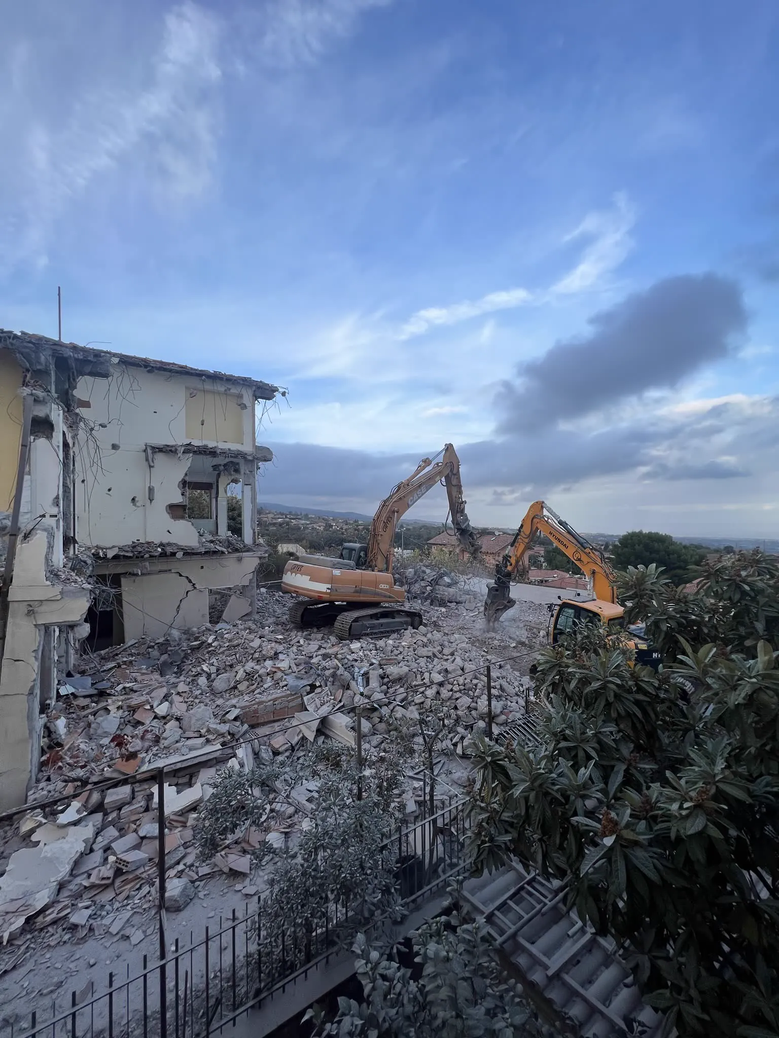 Demolizione di un edificio: due escavatori al lavoro fra le macerie, con la parte ancora in piedi della costruzione a sinistra